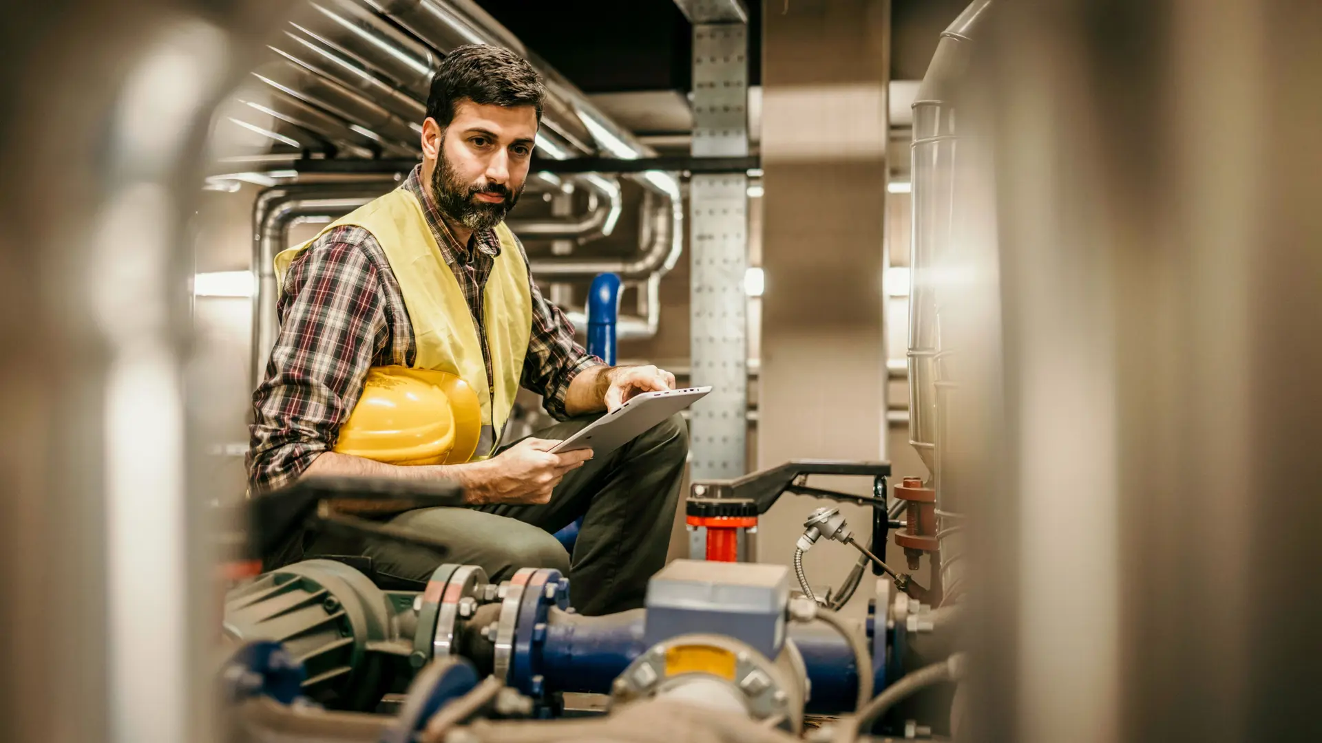 Energieberatung in Unternehmen Mann mit Warnweste überprüft Rohre in einer Fabrik.