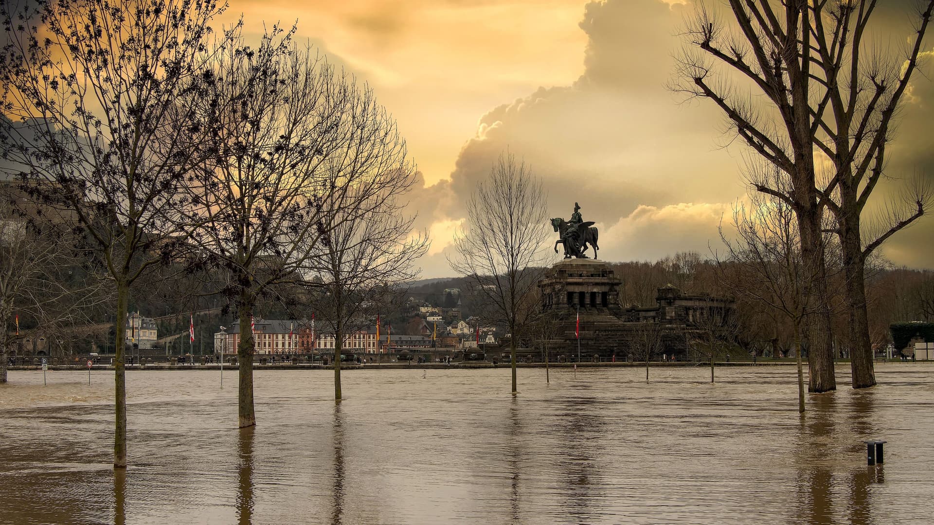 Hochwasser in Koblenz am Deutschen Eck. Im Hintergrund ein dramatischer orangener Himmel mit Wolken,