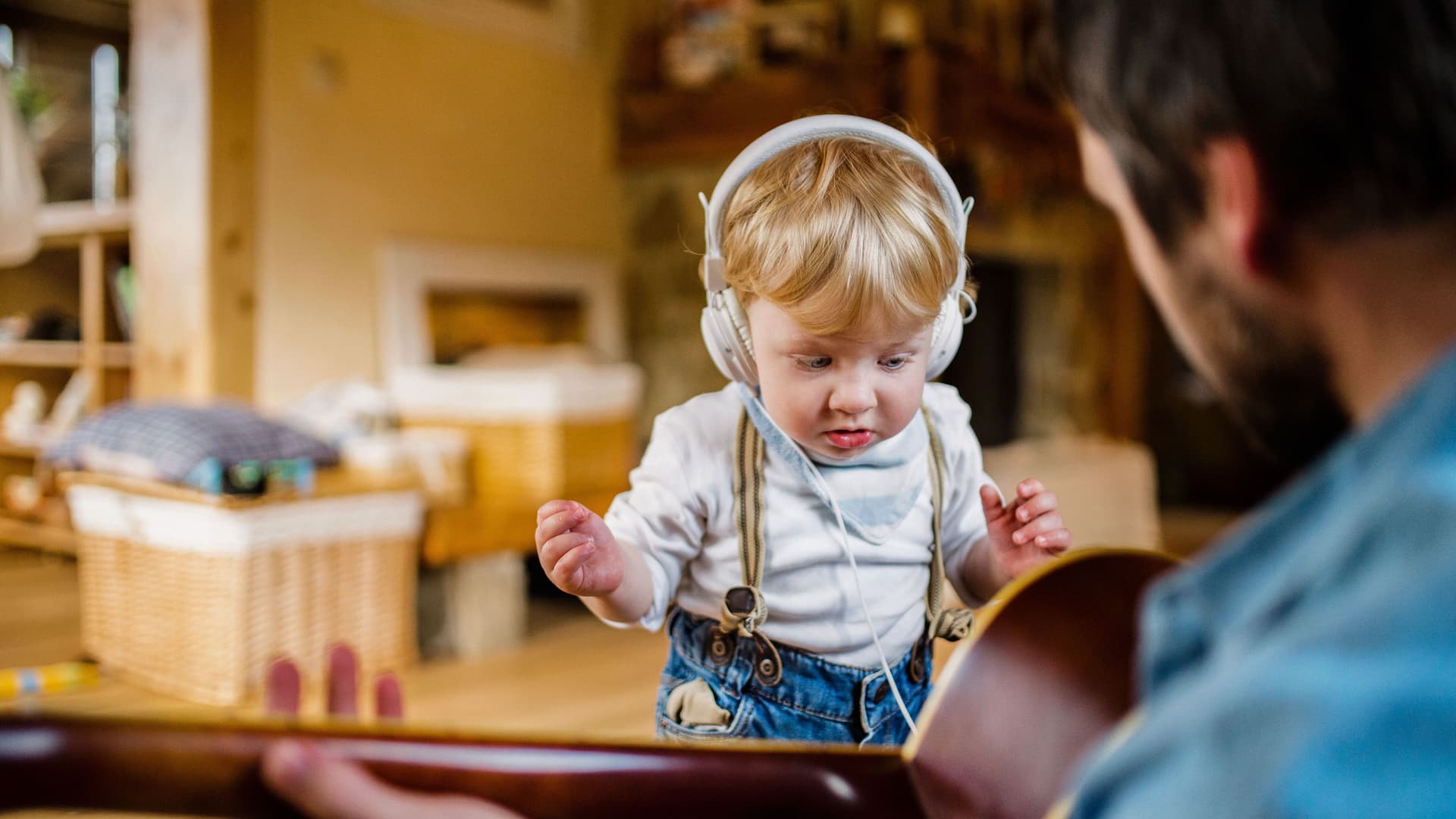 Bild über die Schulter eine Mannes, der Gitarre spielt. Vor ihm steht ein kleiner Junge mit Kopfhörern.