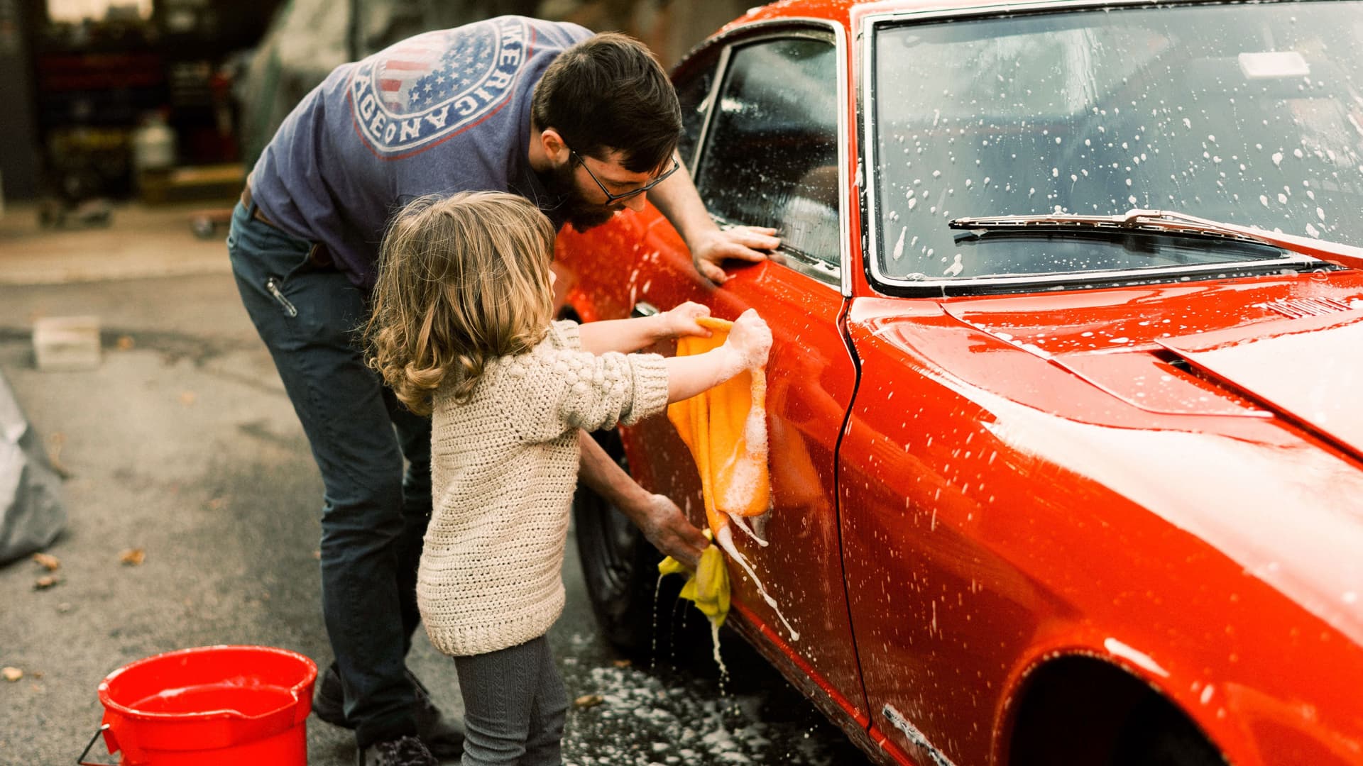 Tochter und Vater reinigen zusammen einen roten Oldtimer.