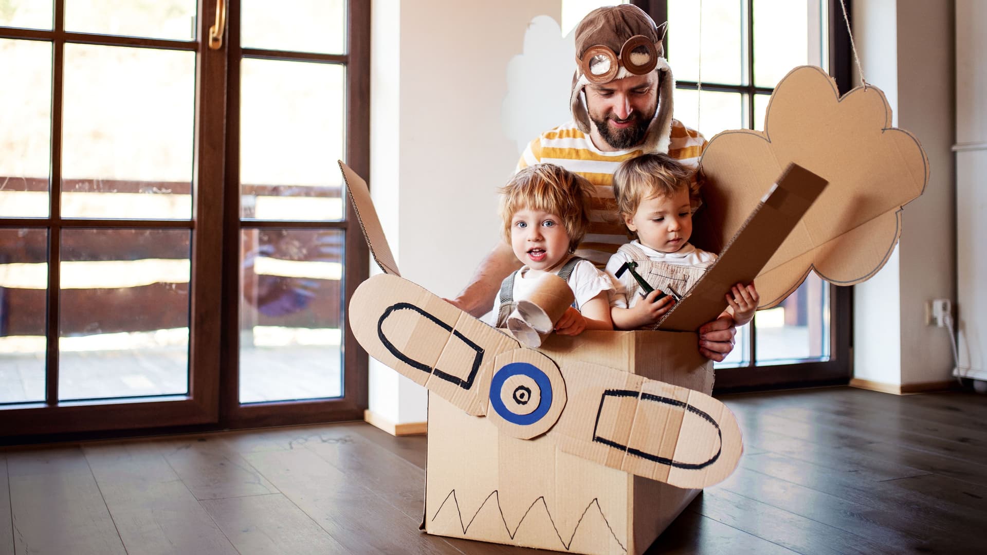 Ein Vater mit Fliegermütze spielt mit zwei Kindern in einem Flugzeug aus Pappe.