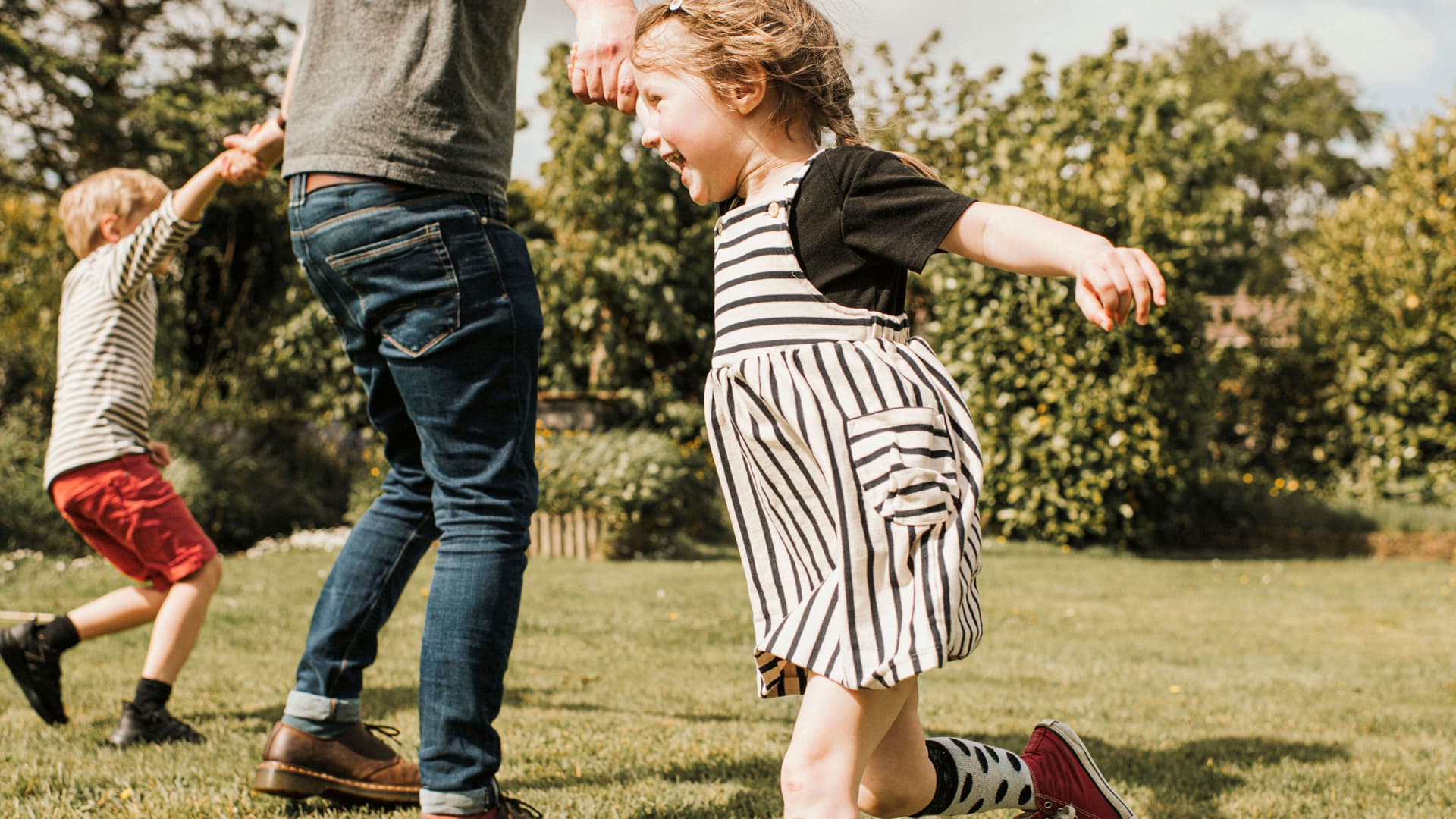 Zwei Kinder toben mit ihrem Vater im Park