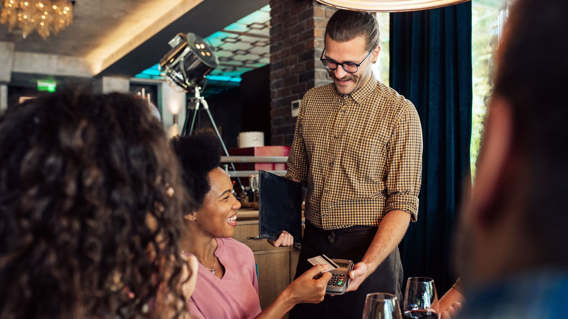 Eine Businessfrau zahlt im Restaurant mit ihrer Visa-Business-Card beim Kellner die Rechnung für ein Geschäftsessen mit mehreren Kollegen.