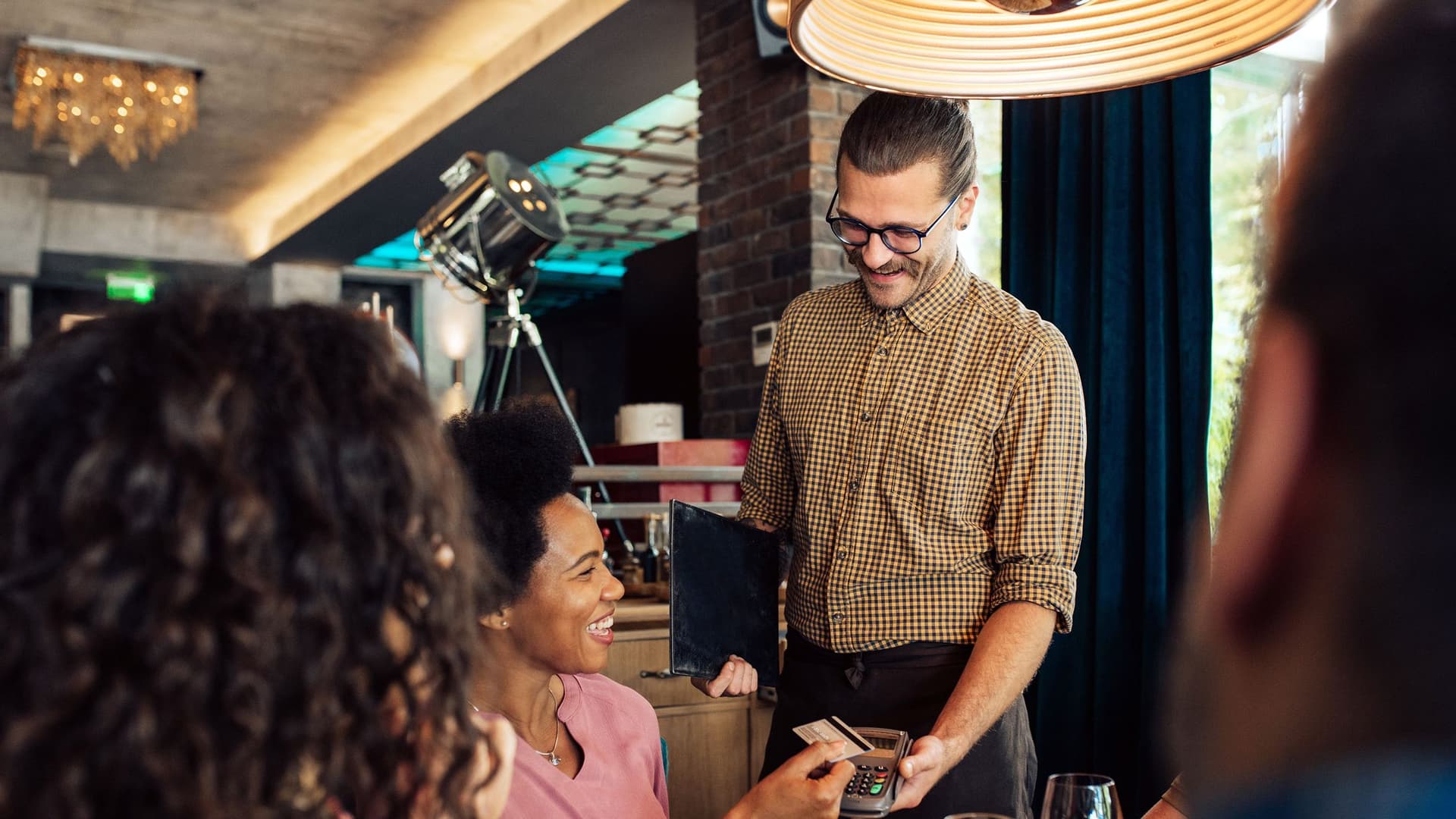 Eine Businessfrau zahlt im Restaurant mit ihrer Visa-Business-Card beim Kellner die Rechnung für ein Geschäftsessen mit mehreren Kollegen.