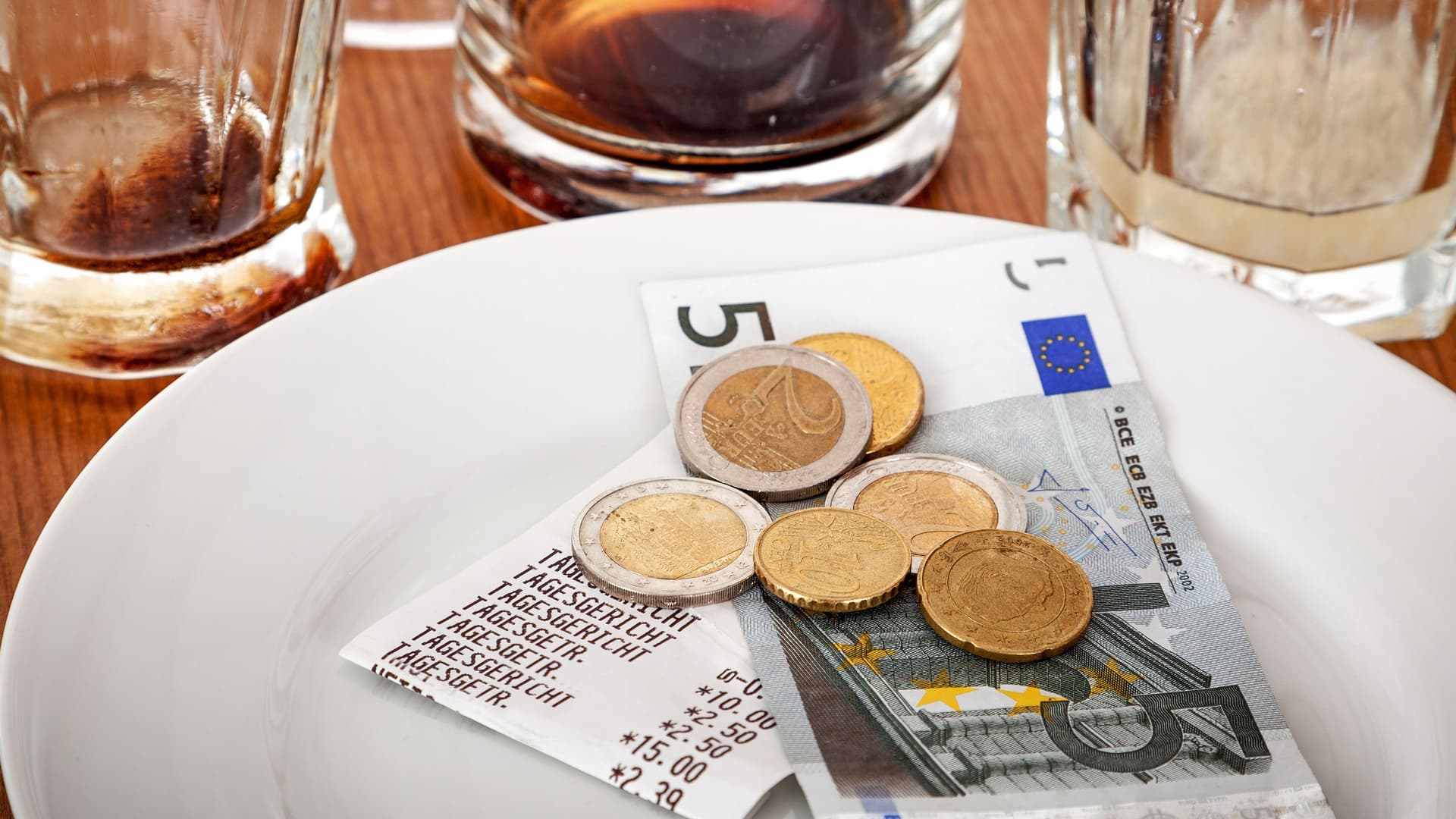 Leere Gläser auf einem Tisch. Bargeld liegt mit Beleg auf einem Teller daneben.