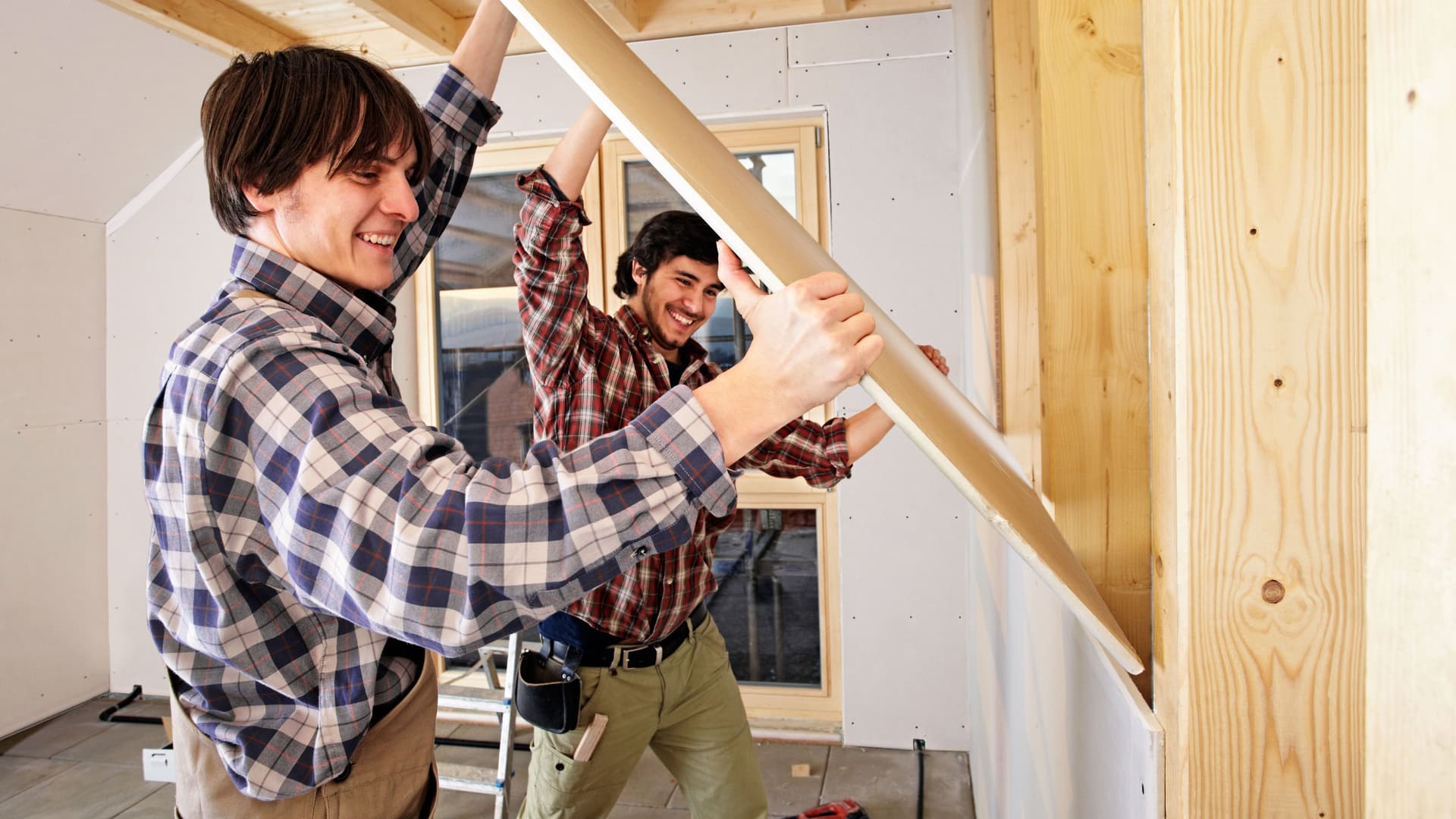 Zwei Männer in Holzfällerhemden, die einen Holzbalken befestigen.