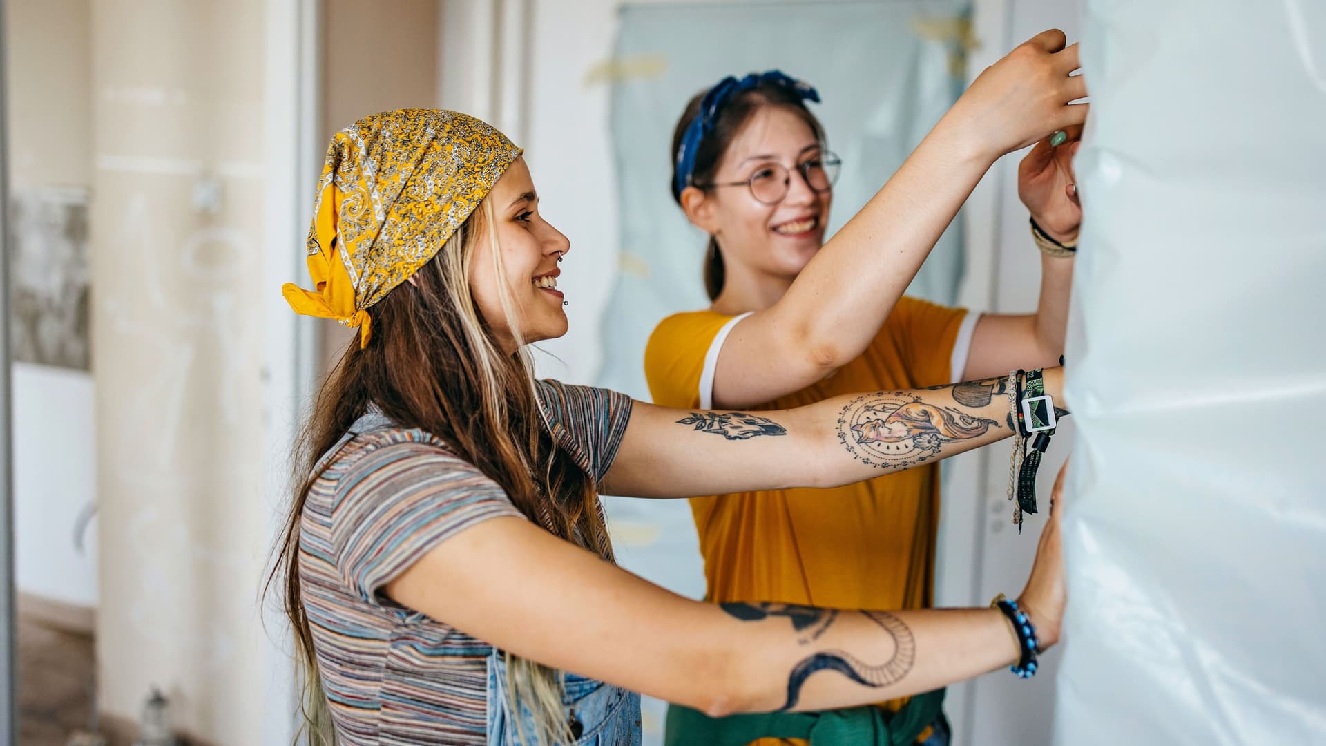 Zwei junge Frauen befestigen Abdeckfolie an einer Wand.