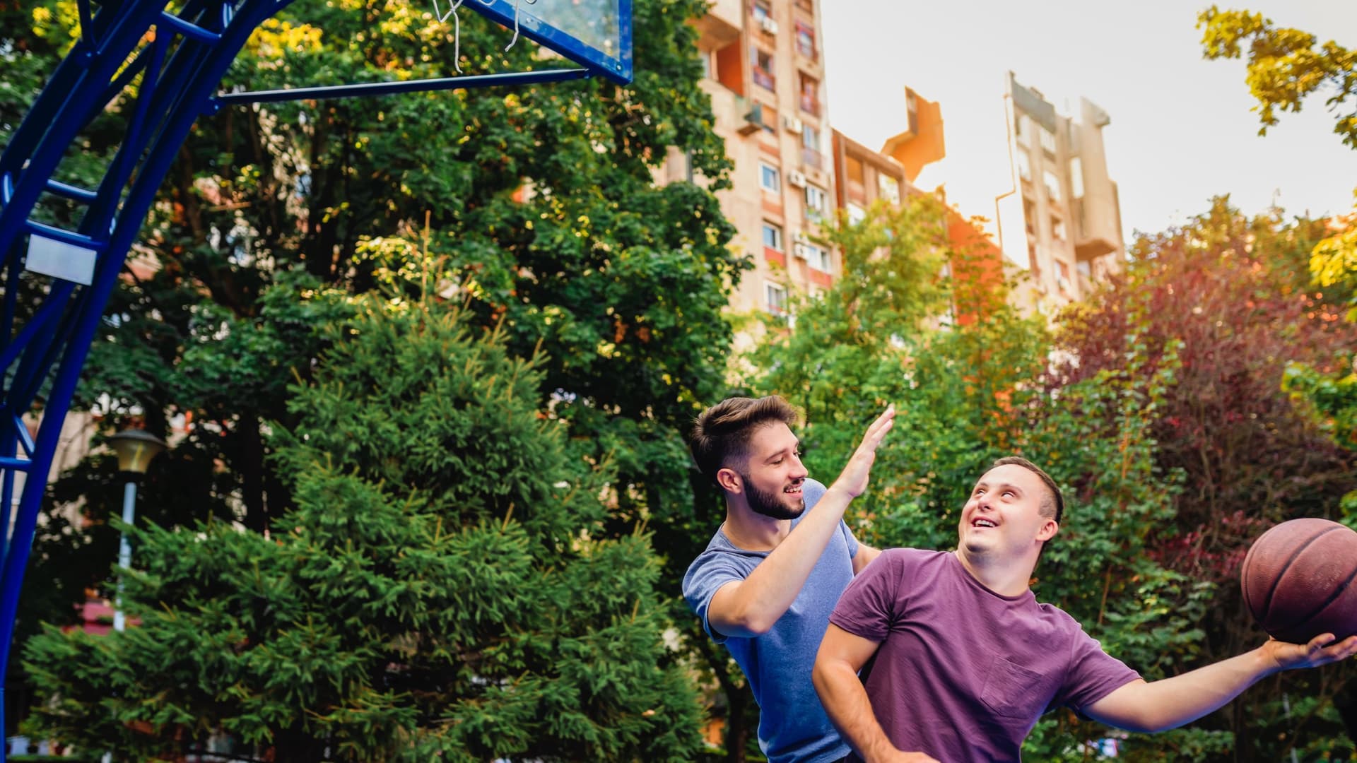 Ein junger Mann mit Down-Syndrom spielt mit einem Freund Basketball.